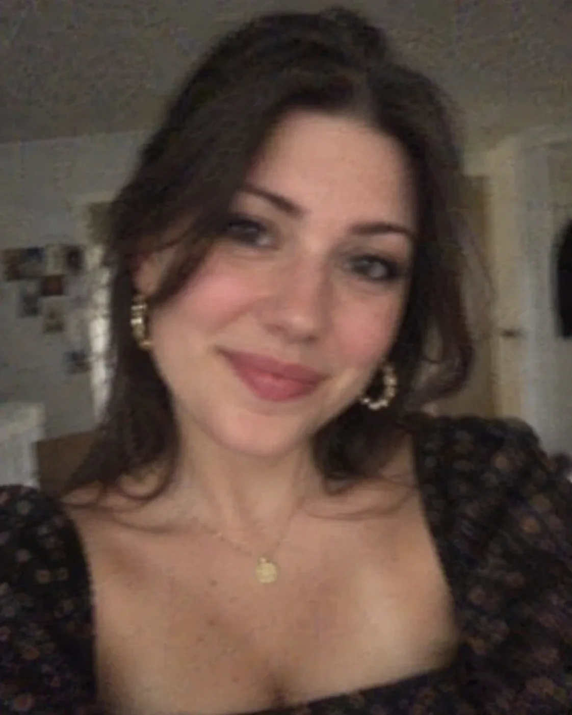 Original: selfie muy borroso de una mujer de pelo castaño con pendientes de aro dorados, collar con medalla y blusa oscura estampada.